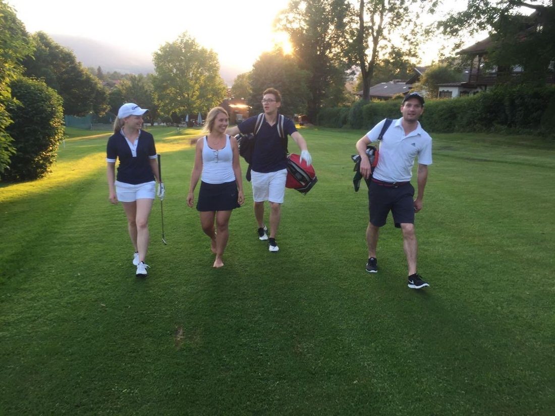 Vier Freunde gehen im Abendlicht über den Golfplatz, die Sonne geht hinter den Bäumen unter.