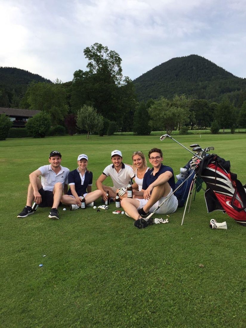 Fünf Freunde sitzen abends auf dem Golfplatz zusammen, mit Bier und Golftaschen.